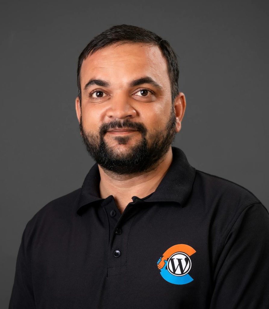 Portrait of a man wearing a black polo shirt with a logo, against a neutral background.